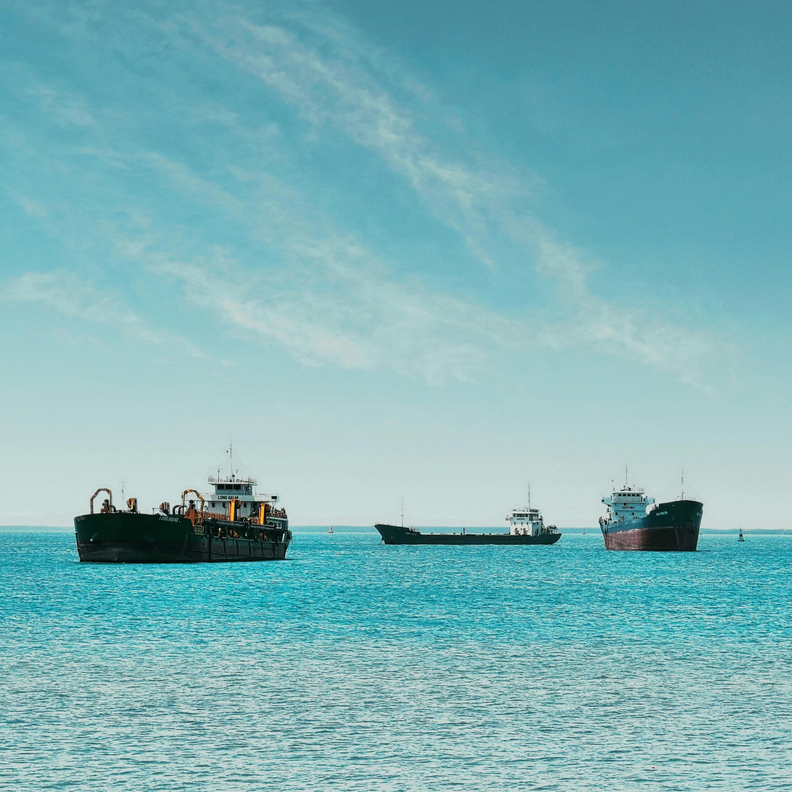 Multiple cargo ships floating serenely on a clear blue sea under a bright sky.